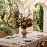 NO. 69 by Nicolíe de Luxe: green artichokes, burgundy pincushions and berry clusters in a crackle-glaze stone urn, styled on a dinner table under a covered villa terrace