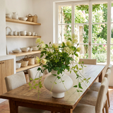 NO. 51 by Nicolíe de Luxe: cream roses, green viburnum and trailing greenery in a round white vase, styled on a farmhouse oak table in a bright villa kitchen-diner