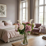 NO. 55 by Nicolíe de Luxe: cream and blush peonies, mauve hydrangeas and white calla lilies in a clear glass vase, styled on an oak table in a mauve-grey villa bedroom