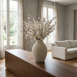 NO. 47 by Nicolíe de Luxe: white cherry blossom branches in a ribbed cream vase, styled on a walnut console in a calm grey-walled villa living room