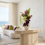 NO. 58 by Nicolíe de Luxe: deep purple orchids, lilac, scabiosa, lime hydrangea and trailing green bells in a cream stoneware vase, styled on a fluted travertine console in a sea-view Marbella living room