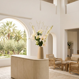 NO. 59 by Nicolíe de Luxe: white lilies, white stock, viburnum and curly willow in a sand-coloured vase, styled on a limestone console in a bright Marbella villa hotel lobby