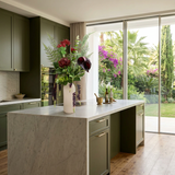 NO. 71 by Nicolíe de Luxe: burgundy protea, crimson chrysanthemums, dark anthurium, ferns and cascading berry strands in a white cylindrical vase, styled on a marble kitchen island in a Marbella villa kitchen