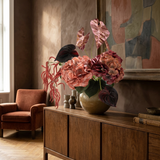 NO. 76 by Nicolíe de Luxe: coral and dusty rose hydrangeas, burgundy anthuriums and cascading coral amaranthus in a smoked glass vase, styled on a walnut sideboard in an art-filled sitting room
