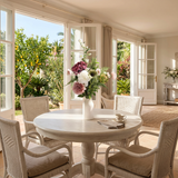 NO. 73 by Nicolíe de Luxe: blush carnations, mauve hydrangea, ivory peony, green artichoke, white blossoms and fern in a white bottle vase, styled on a round breakfast table in a Marbella villa garden room