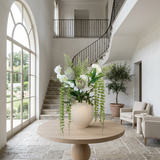 NO. 28 by Nicolíe de Luxe: king proteas, white hydrangeas and blooms, ferns and cascading string-of-pearls in a cream stoneware vase, styled on a round oak table in a double-height villa foyer