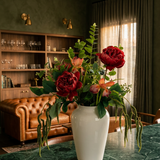 NO. 64 by Nicolíe de Luxe: deep red roses, tiger irises, eucalyptus and cascading amaranthus in a white vase, styled on a green marble counter in a moody villa lounge